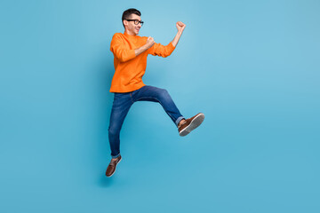 Fototapeta na wymiar Full length profile portrait of astonished handsome guy fists up jump celebrate isolated on blue color background