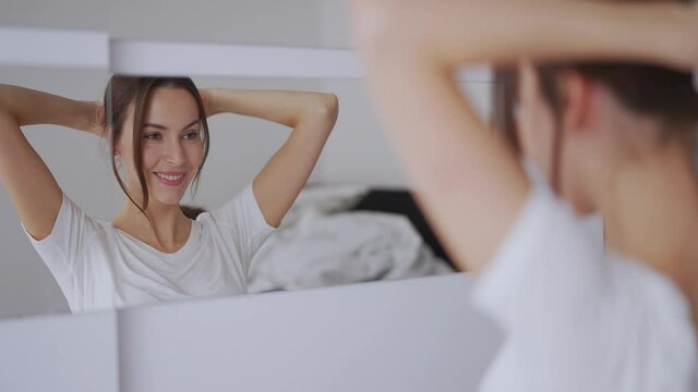 Glad woman doing hair near mirror