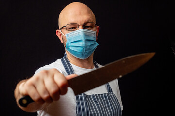 Studio portrait of a bald butcher of fishmonger on a dark background. Meat industry and health care concept. The model in white t shirt and classic blue white stripe apron wearing glasses in his 40s