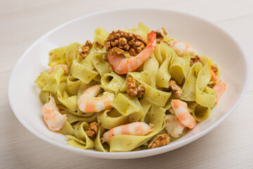 Close up of Fettuccine pasta with shrimp, pesto sauce, walnut on white plate ready to eat. Mediterranean cuisine.