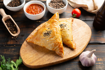cutting board with delicious baked samosas on wooden background