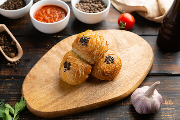 cutting board with delicious baked samosas on wooden background