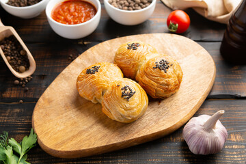 cutting board with delicious baked samosas on wooden background