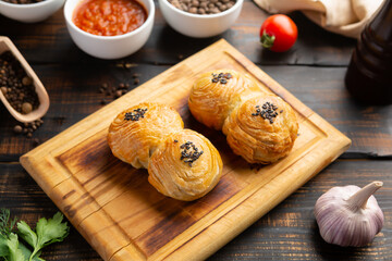 cutting board with delicious baked samosas on wooden background