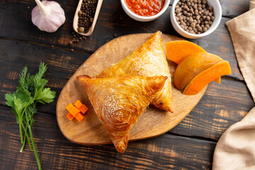 cutting board with delicious baked samosas on wooden background
