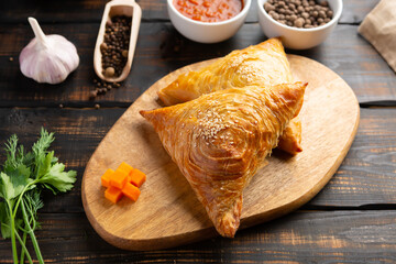 cutting board with delicious baked samosas on wooden background