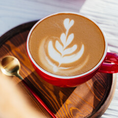 cappuccino in a red cup and a red spoon on a wooden board