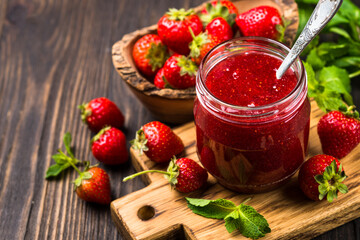 Strawberry jam in the glass jar at wooden table.
