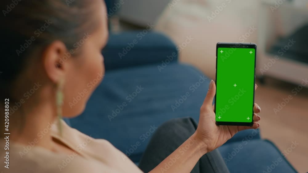 Aufkleber caucasian female sitting on sofa in living room while socializes on internet app using phone with mo