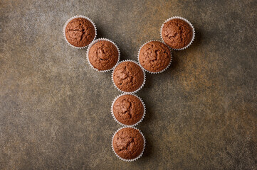 Chocolate homemade cupcakes laid out in the form of letter Y on wooden background, copy space, top view