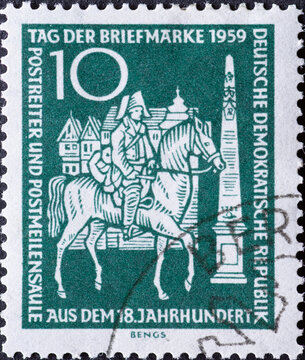 GERMANY, DDR - CIRCA 1959 : a postage stamp from Germany, GDR showing a mail rider on horseback with houses, post miles pillar. Postage Stamp Day 1959