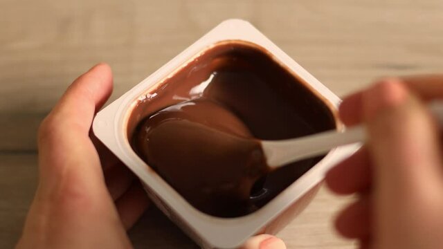 Close up of man hands take a delicious chocolate mousse or pudding with spoon in a plastic jar