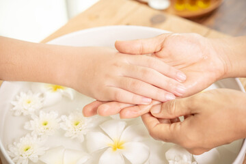 Beautician massaging hand of female spa salon client. Spa treatment and product for female feet and hand spa. white flowers in ceramic bowl with water for aromatherapy at spa.