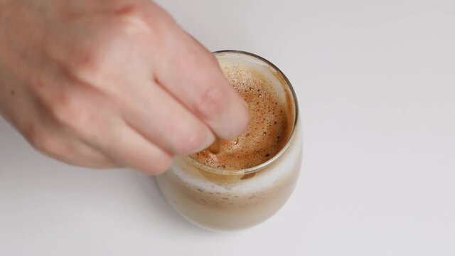 Making morning coffee with milk, stirs sugar in a cup. Woman person hand stirring latte coffee with glass spoon on white table