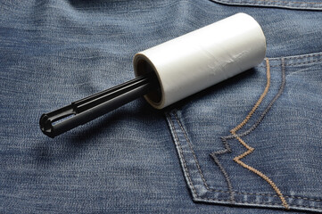Naklejka premium A sticky, roller-coiled garment brush rests on dark jeans.
