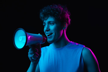 Young man with megaphone isolated on dark multicolored background in neon light - obrazy, fototapety, plakaty