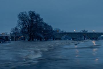 Historical landmark stone bridge in Regensburg, Bavaria, Germany at night with high water flood...