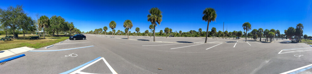 Fototapeta premium Almost empty huge car parking along a park with palms - Panoramic view