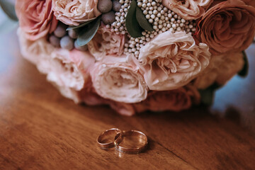 Gold wedding rings lie on a wooden table, against the background of the bride's bouquet of roses. Wedding concept.