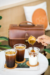 A hand pouring a cup of hot coffee after brewed into a glass of milk with the beautiful coffee decorated background with a brown bag.