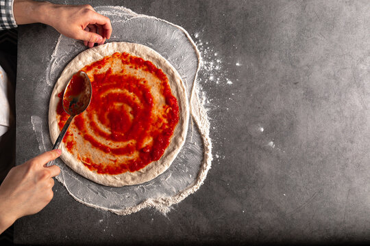 Making a pizza spreding tomato sauce on the dough on the grey concrete background