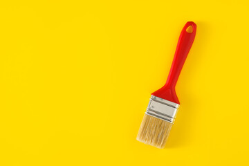 Paintbrush with red handle on yellow background.