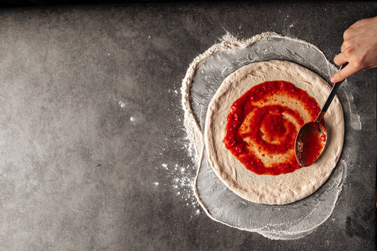 Making a pizza spreding tomato sauce on the dough on the grey concrete background - Powered by Adobe