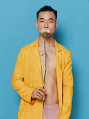 Asian man with flower in his hands and yellow jacket blue background naked torso