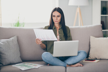Fototapeta na wymiar Portrait of charming skilled focused girl sitting on divan using laptop reading documents working remotely at home house flat indoor