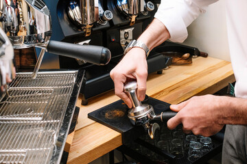 Close-up view of unrecognizable male barista compressing ground coffee with tamper while making espresso