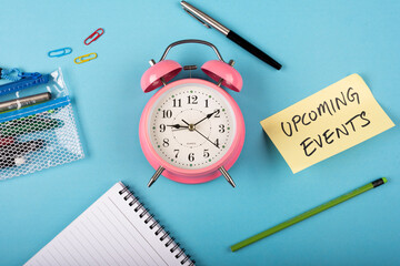 A table clock with words Upcoming events Written on a yellow sticky note and Pen with other elements on a blue background