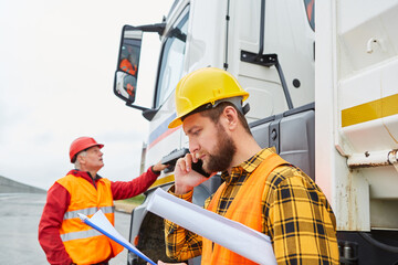 Arbeiter telefoniert mit Smartphone vor einem LKW