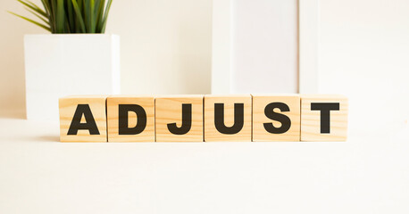 Wooden cubes with letters on a white table. The word is ADJUST. White background.