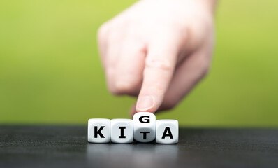 Hand dreht Würfel und ändert die Abkürzung KITA (Kindertagesstätte) in KIGA (Kindergarten).