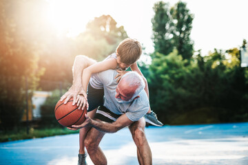 Grandfather and his grandson enjoying in beautiful sunny day and playing basketball.