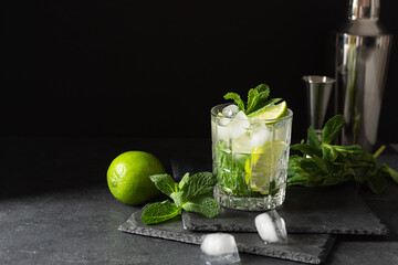 Refreshing summer mojito cocktail with ice cubes, fresh mint and lime on black.