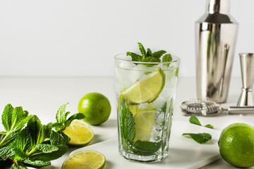 A glass of refreshing summer mojito cocktail with ice cubes, fresh mint and lime on white.