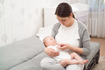 Young mother holding her newborn child. Mom nursing baby. Woman and new born boy relax in a white bedroom.