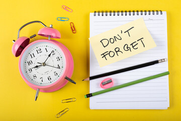 Fototapeta na wymiar A table clock with Don't forget words Written on a sticky note with notepad pencil and other elements on a Yellow background.