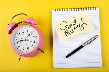 A table clock with Good morning words Written on a sticky note with notepad and other elements on a Yellow background