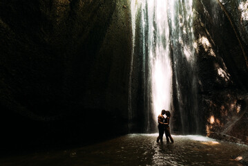 Beautiful couple in a cave with a waterfall. Athletic man and woman under the streams of a waterfall. A sexy couple under a tropical waterfall in twilight light. Tukad Chepung Waterfall. Copy space