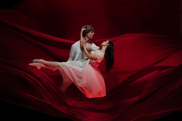 Feelings. Young and graceful ballet dancers on red cloth background in classic action. Art, motion, action, flexibility, inspiration concept. Flexible caucasian couple with billowing red waves.
