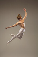Muscular. Young and graceful ballet dancer isolated on studio background in flight, jump. Art, motion, action, flexibility, inspiration concept. Flexible caucasian ballet dancer, moves in glow. - obrazy, fototapety, plakaty