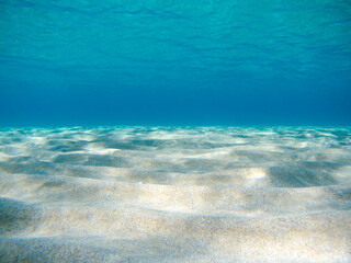 Underwater view on sand sea bottom close-up in sun beam reflections in clear water of Ionian Sea in Greece. Diving azure wild sea water