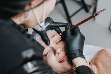 Fototapeta na wymiar Eyebrows microblading concept, eyebrow permanent makeup procedure. Beauty expert is wearing shiled and protective face mask due to Coronavirus pandemic.