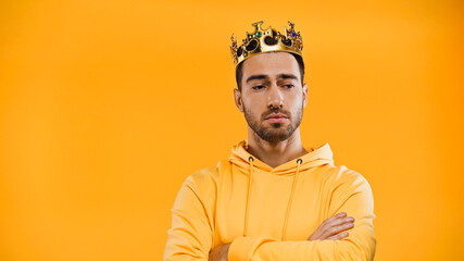 man in golden crown standing with crossed arms isolated on yellow