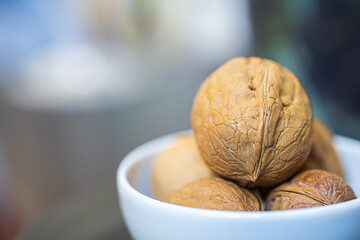 Heap, pile of whole walnuts in a round-shaped shell lie in a small white plate on a blurred bokeh background. Place for text