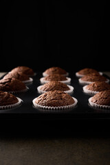 Homemade chocolate cupcakes in baking paper forms on wooden background, selective focus, close up, vertical orientation