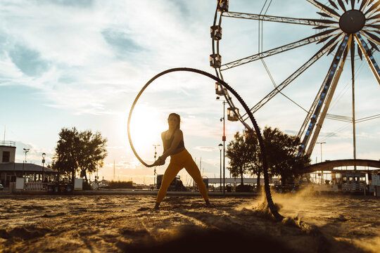Woman doing fitness workout at a beach on sunset - Girl doing workout using two battle ropes on the beach