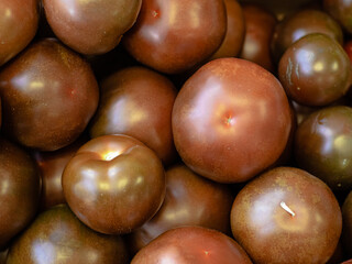 Heap, pile of dark red ripe kumato tomatoes lie in a store, supermarket. Seasonal vegetables are on top of each other